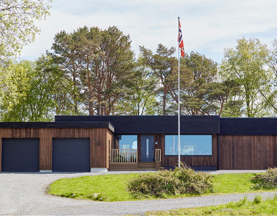 Et bilde av husets forside med skog i bakgrunn.