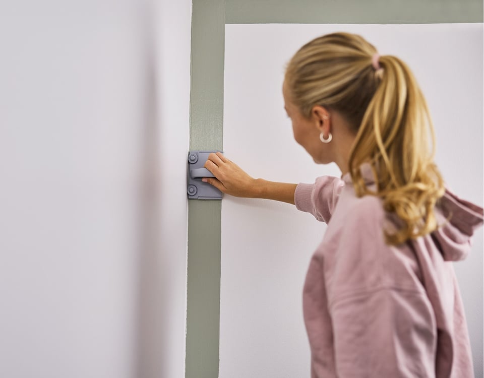 En dame som bruker Jotun Rolling Pad til å male veggen langs et hjørne.