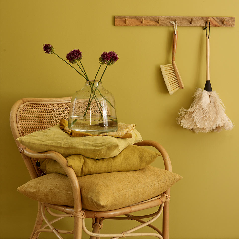 Kurvstol med to gule puter foran gul vegg.