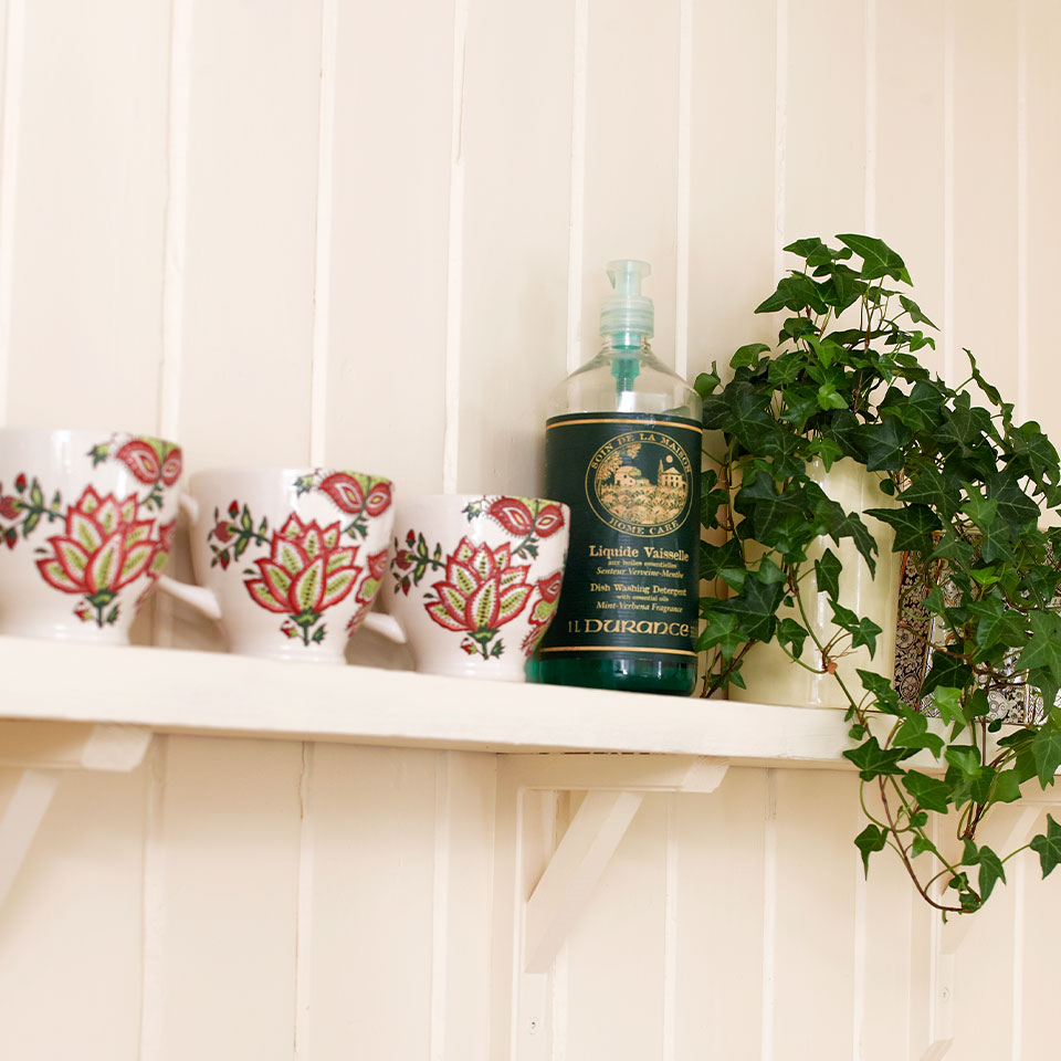 Hylle med tre kopper, såpebeholder og grønn plante