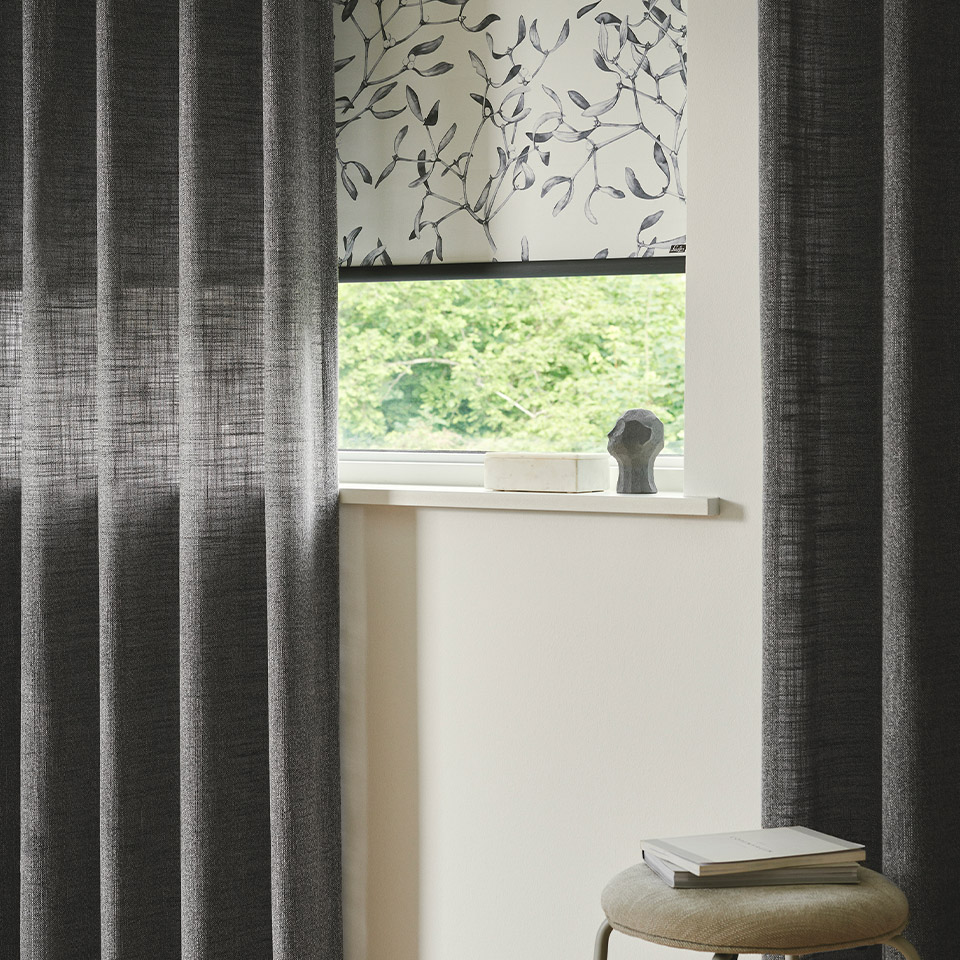 Lys rullegardin med mørkt organisk mønster, i kombinasjon med dekorative mørke hengende gardiner