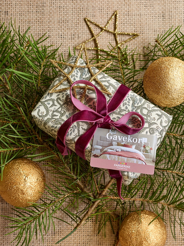 En gave som ligger på granbard med et gavekort på toppen.