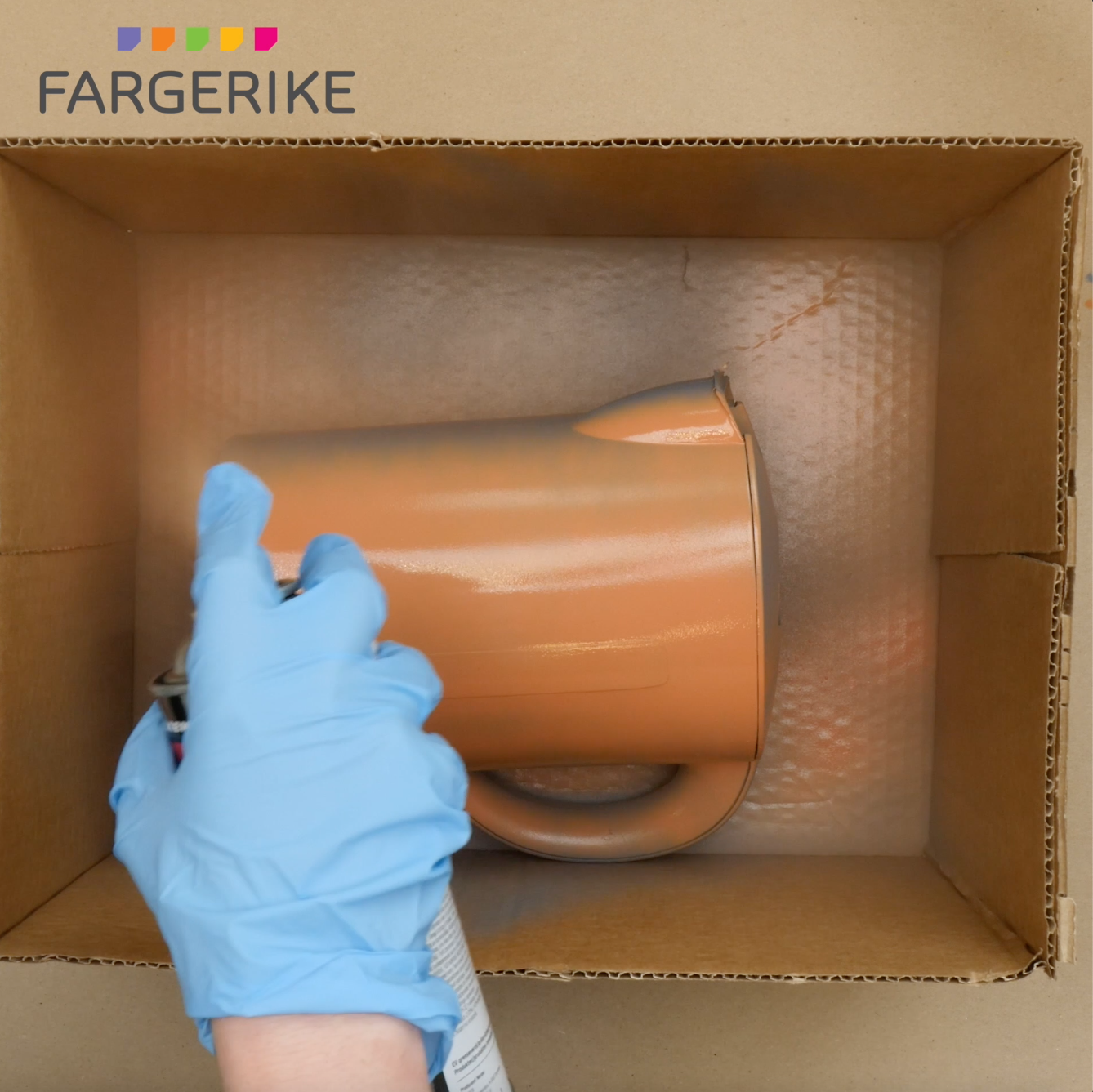 Bilde av en hånd med hanske som spraymaler en vannkoker