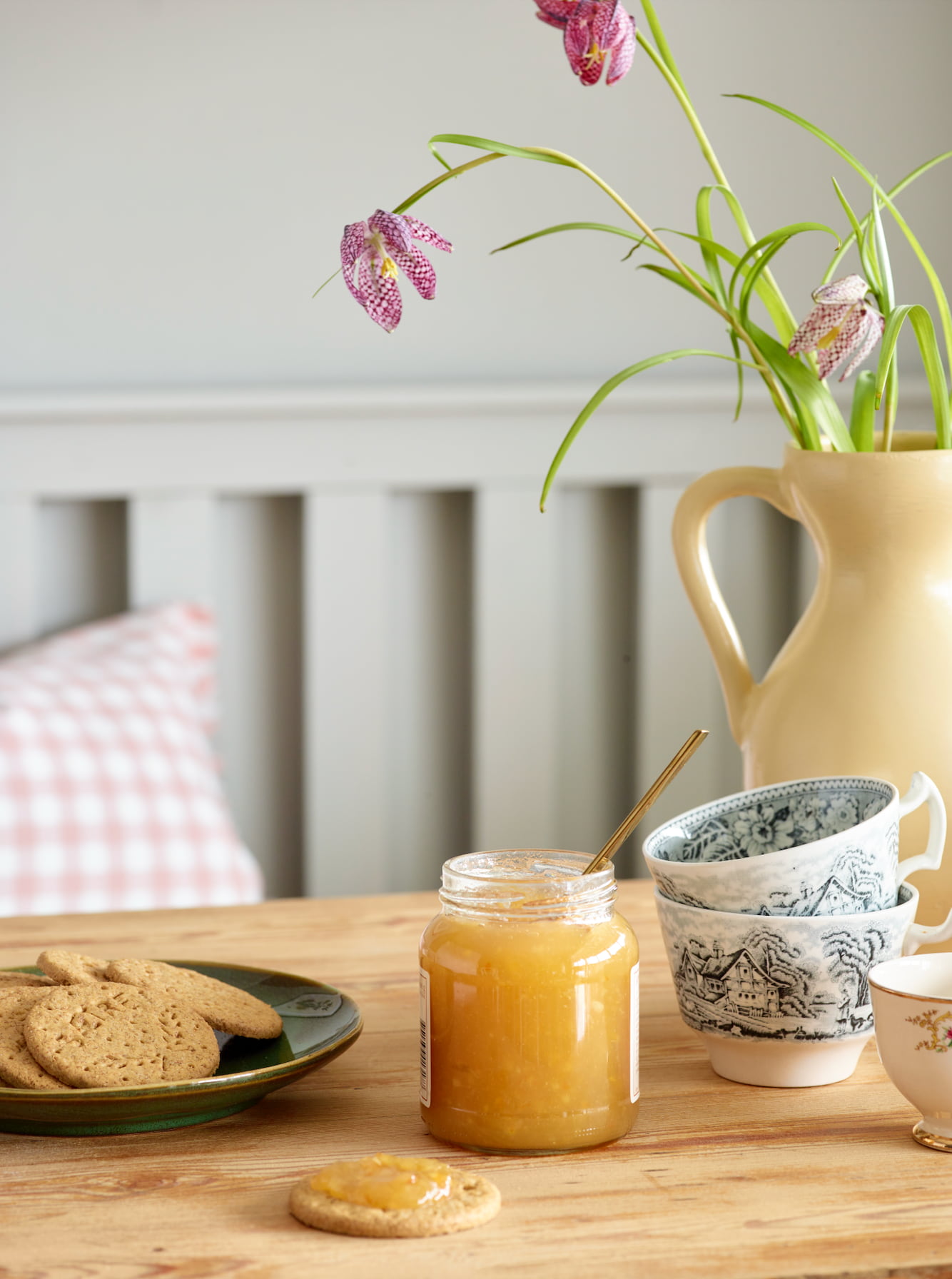 Kjeks og syltetøy på et bord med kopper og en vase med blomster