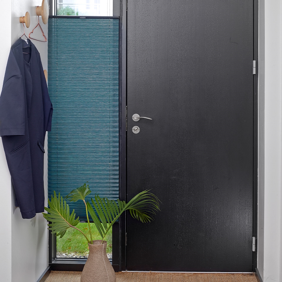 Vindu ved ytterdør med turkisfarget plisségardin