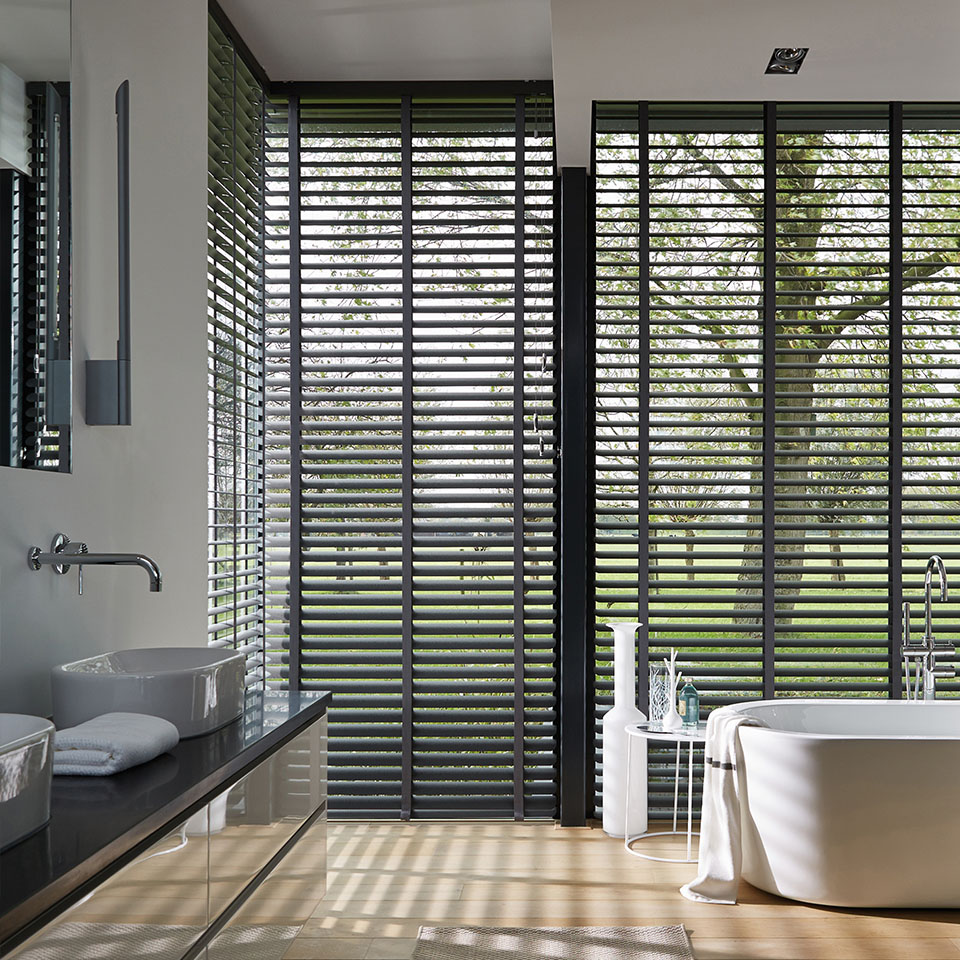 Baderom med store vindusflater, dekket med aluminiumspersienner i mørk gråtone for lysinnslipp men likevel privatliv
